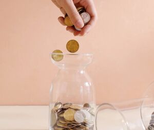 A person putting coins into a jar.